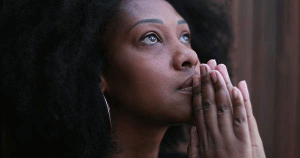 Young, African American woman praying with tears in her eyes